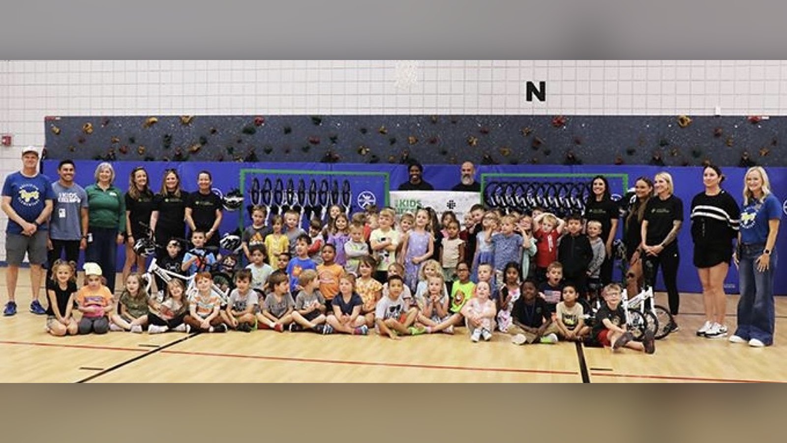 Niños y educadores posando en un gimnasio escolar con bicicletas de equilibrio