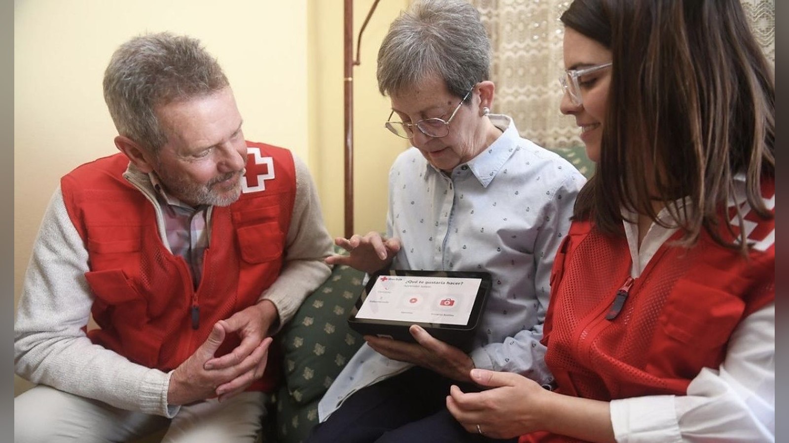 Un voluntario y una voluntaria de Cruz Roja enseñan a una mujer mayor a usar una tableta